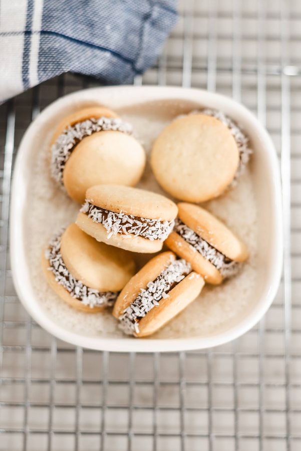 Alfajores de maicena, sandwichkoekjes met door kokos gerolde randen, in een klein wit schaaltje