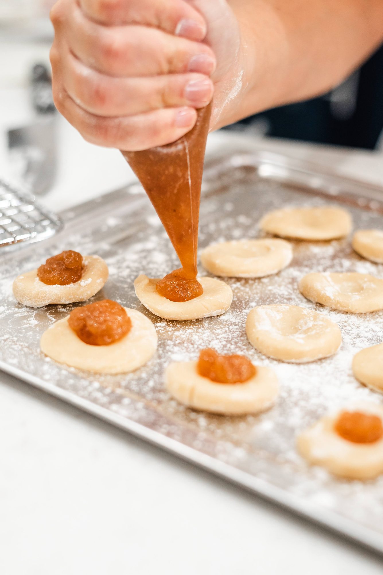 Handen die dulce de leche op rondjes koekjesdeeg spuiten op een bakplaat